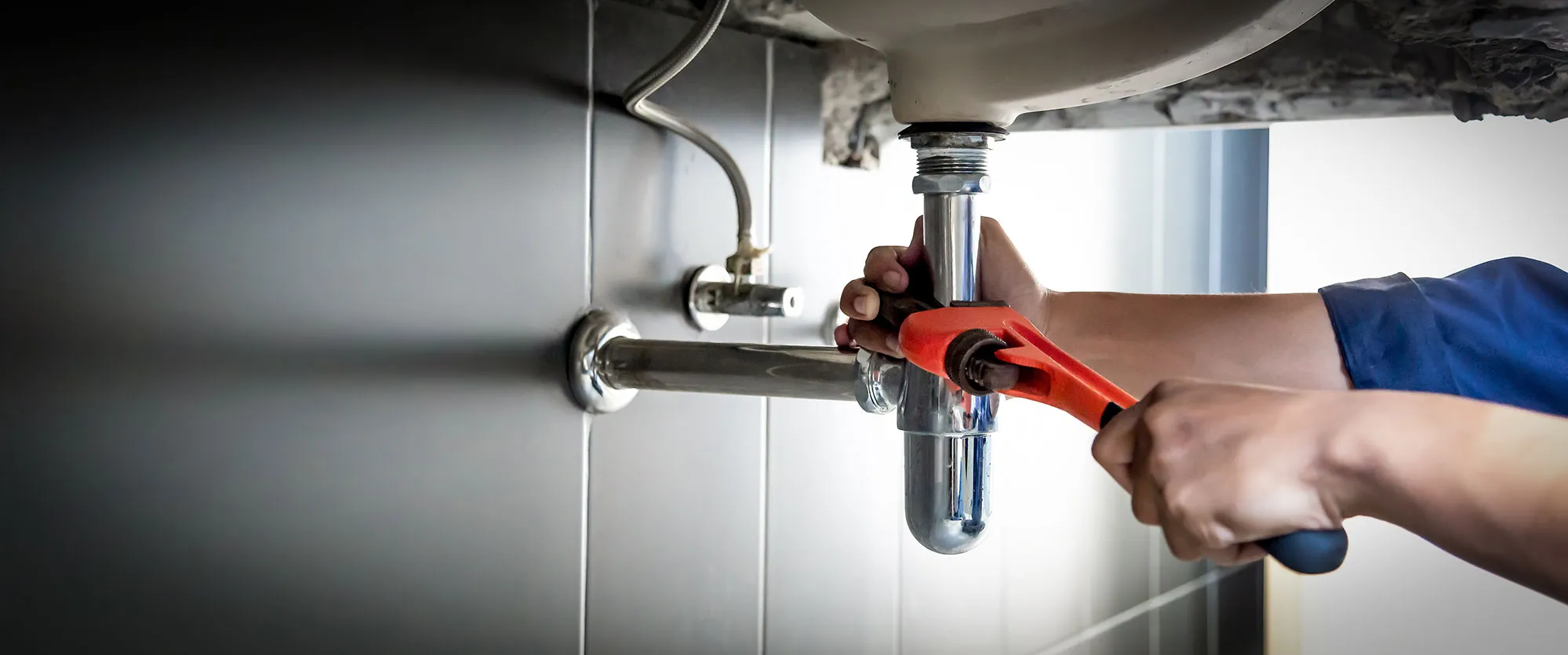 A person holding a wrench in front of a sink.