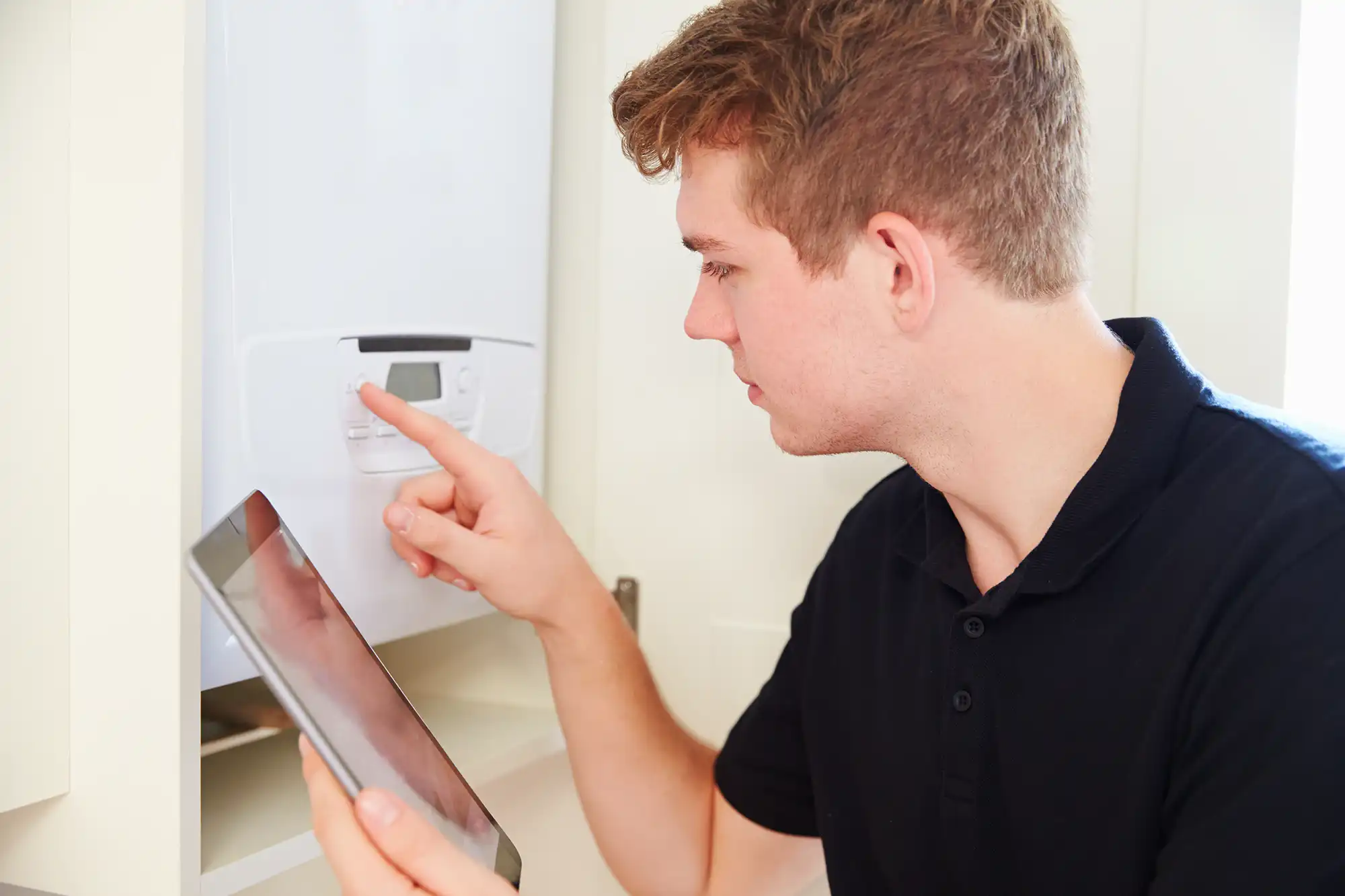 A man looking at an electronic boiler in a kitchen.