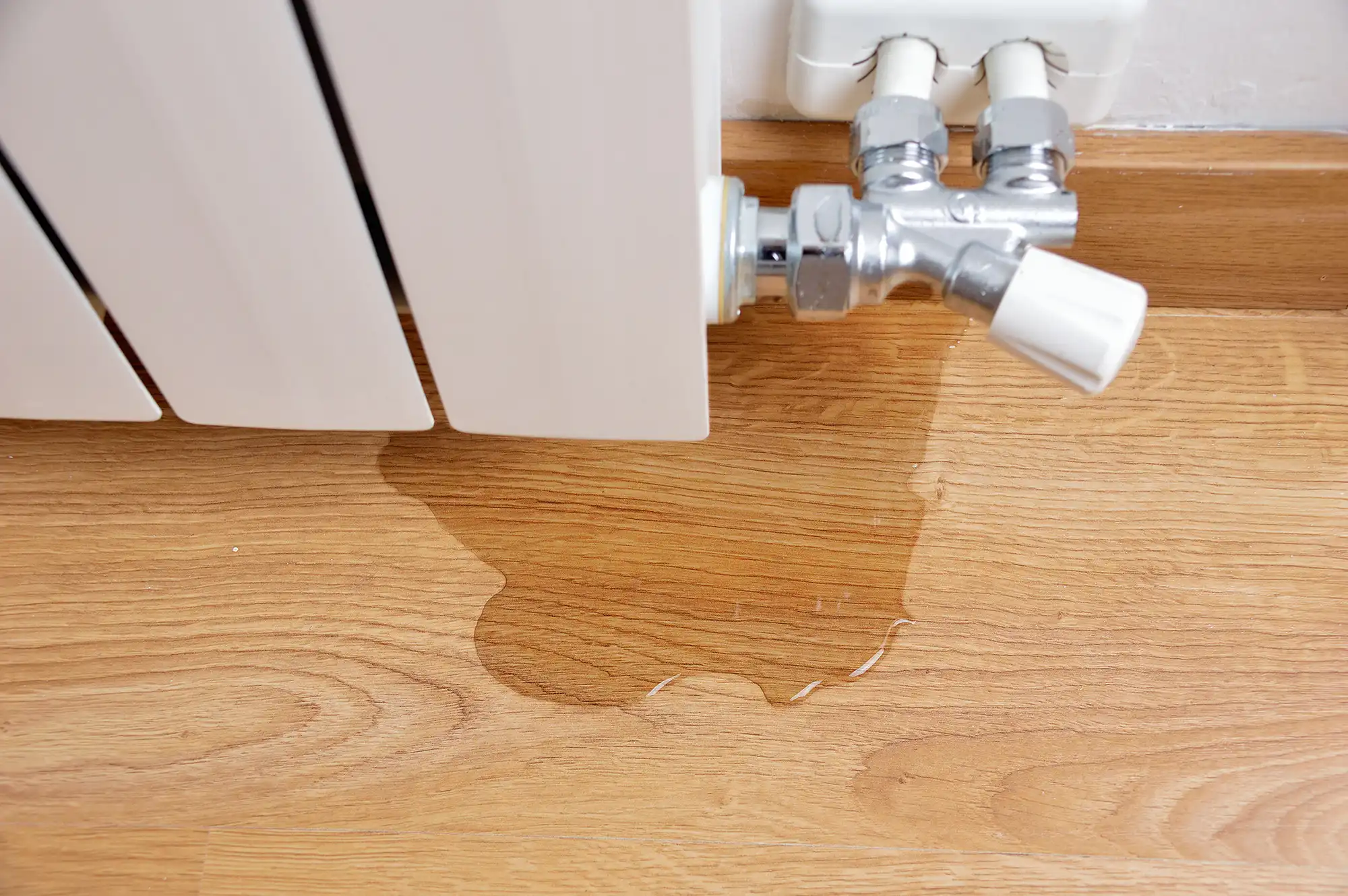 A close up of a leaking radiator on a wooden floor.
