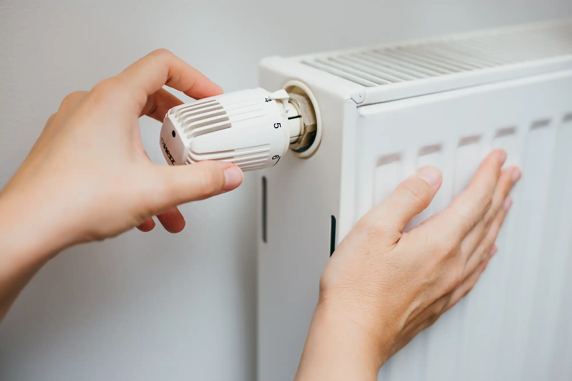 A person adjusting a heater on a wall.